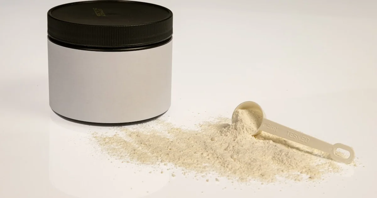 A tin of infant formula powder with a measuring scoop, spilled powder beside it