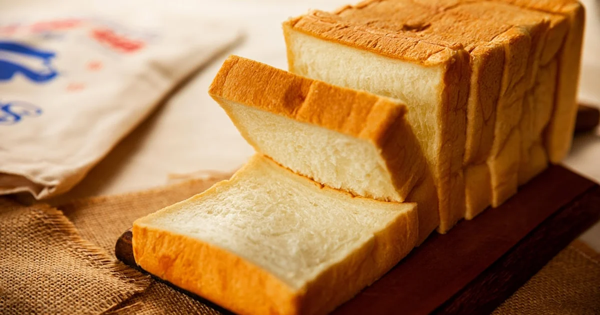 Sliced white bread loaf on a wooden board with a flour sack and burlap cloth