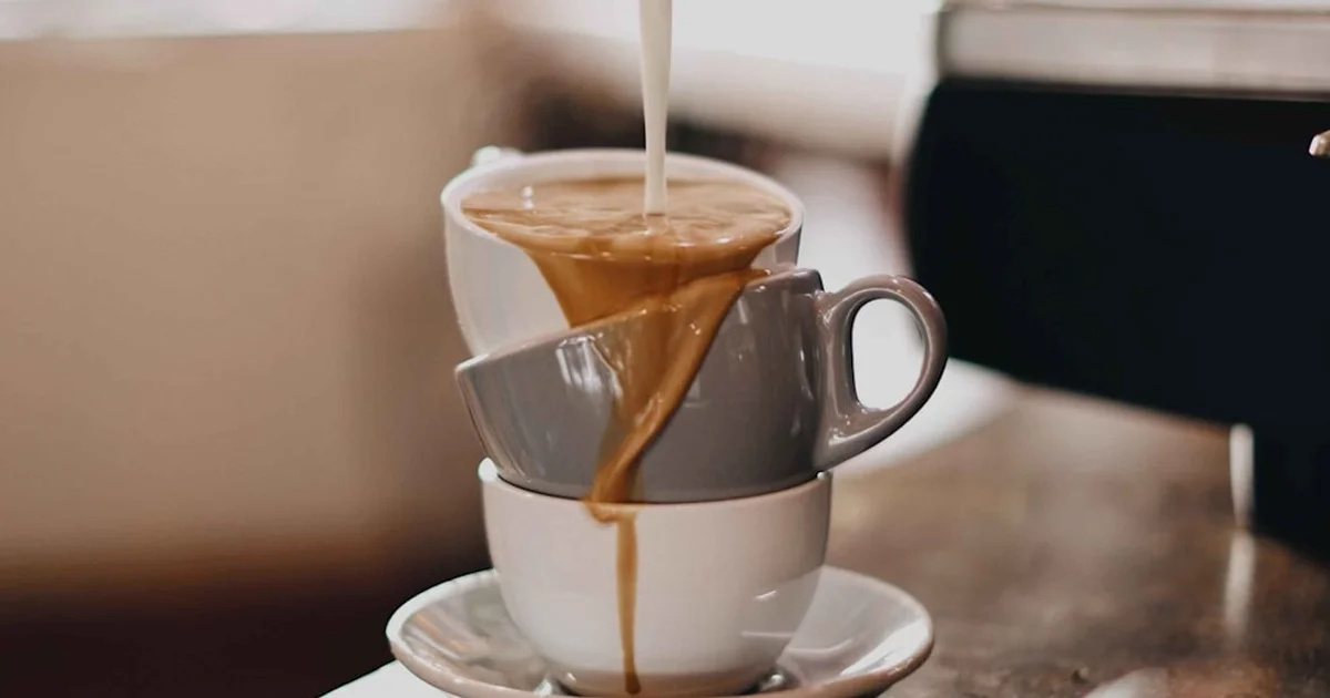 Cream pouring into a stack of coffee cups on a saucer