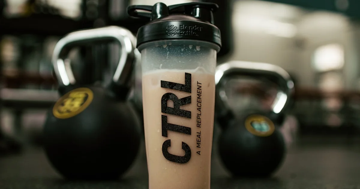 A ready-to-drink meal replacement shaker bottle beside gym kettlebells