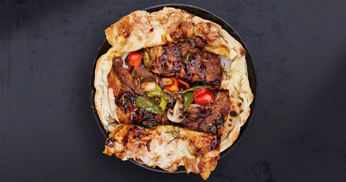 Grilled meat, peppers, and mushrooms wrapped in flatbread on a dark plate, overhead view