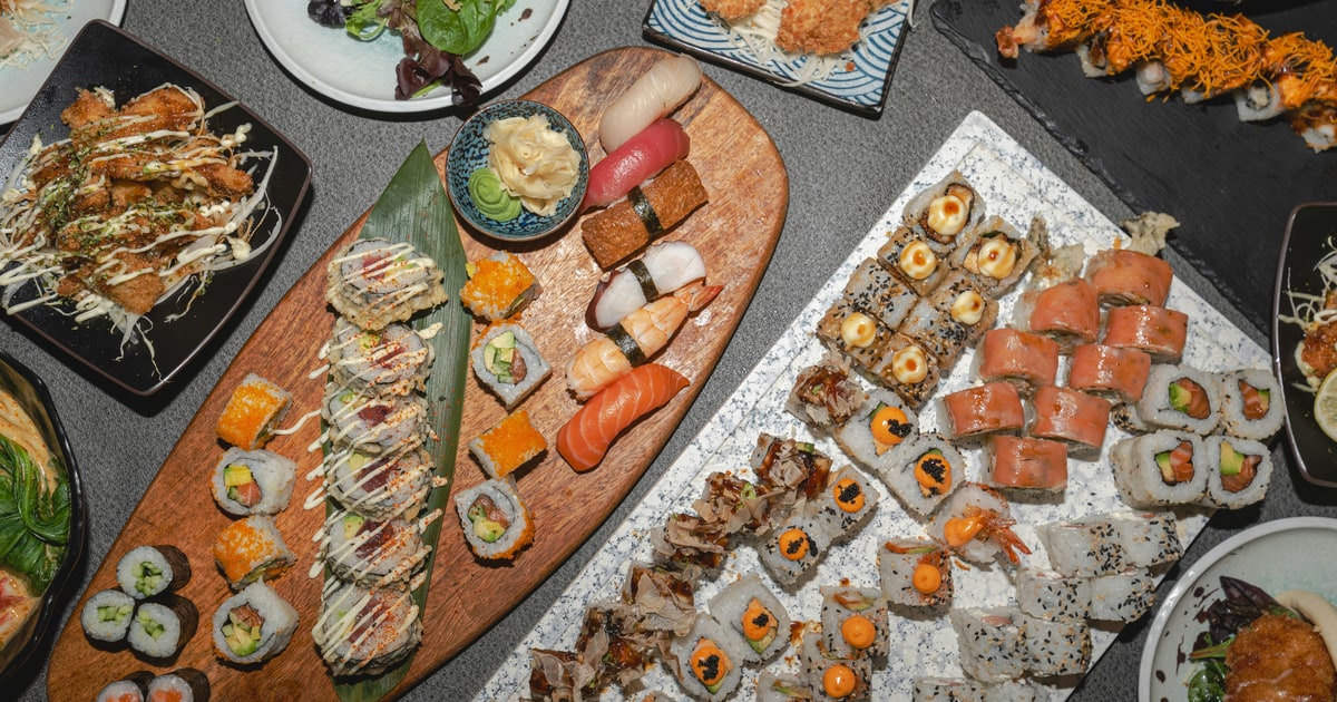 Assorted sushi rolls and nigiri displayed on a wooden board with soy sauce and wasabi