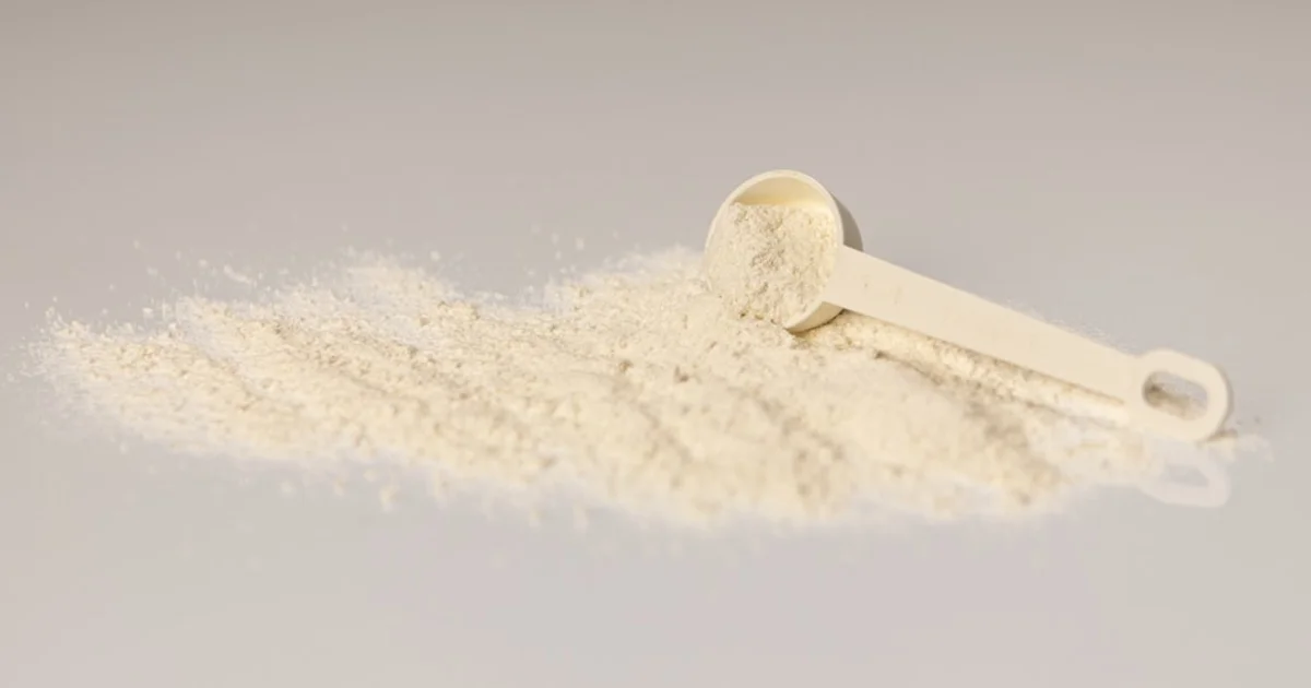 White collagen supplement powder spilled beside a plastic measuring scoop