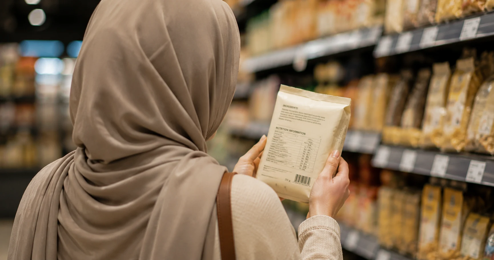 Muslim shopper reading a packaged food label in a supermarket aisle
